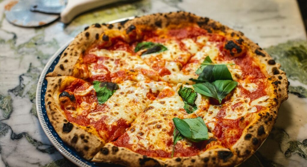 Pizza artesanal de fermentação lenta saindo fumegante do forno a lenha com queijo derretido e manjericão fresco